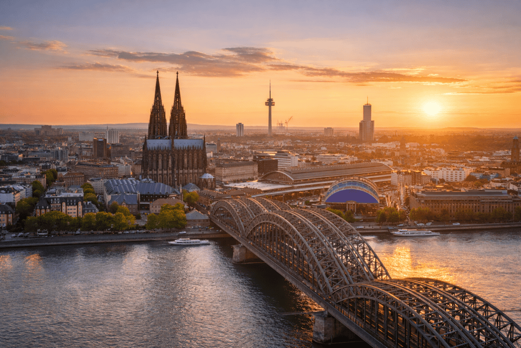 Blick auf den Kölner Dom und den Rhein bei Sonnenuntergang mit Altstadt und Rheinbrücken im Querformat.